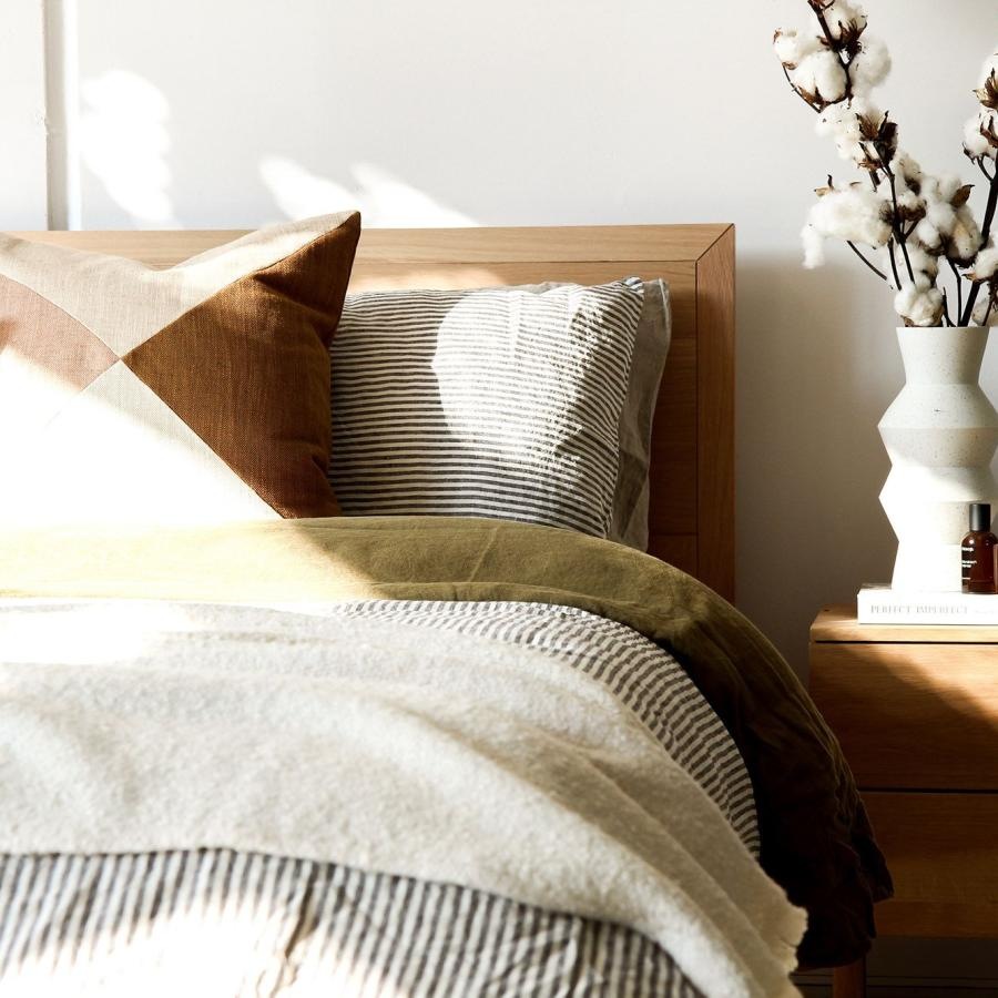 swath of sunlight shines across a well made bed and bedside table with a vase of cotton plants